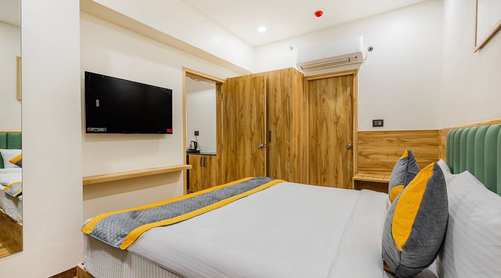 Lemonridge Hotels, KPHB | Hotel room featuring a bed with a grey and yellow runner, a TV, and wooden furniture. Comfortable stay.